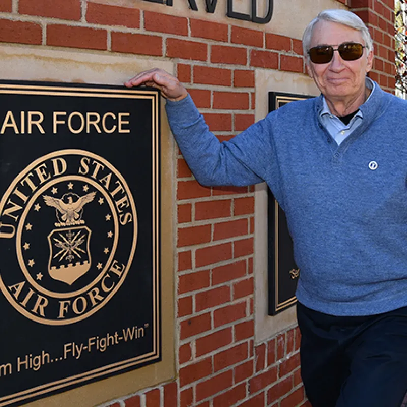 Veteran staff member beside Air Force plaque on brick wall